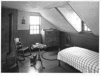 SA0523 - Exhibit at Fruitlands Museum, Harvard, Mass., showing No. 1 Shaker House: sisters' retiring room, bed, chest of drawers, rocking chair, table, stove, and rug. Identified on the back., Winterthur Shaker Photograph and Post Card Collection 1851 to 1921c